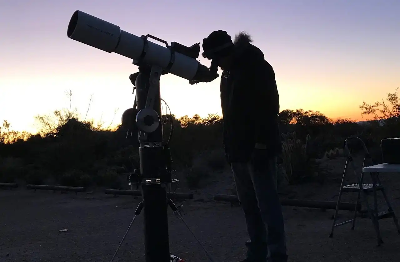 A member looking through a telescope eyepiece at sunset in the desert