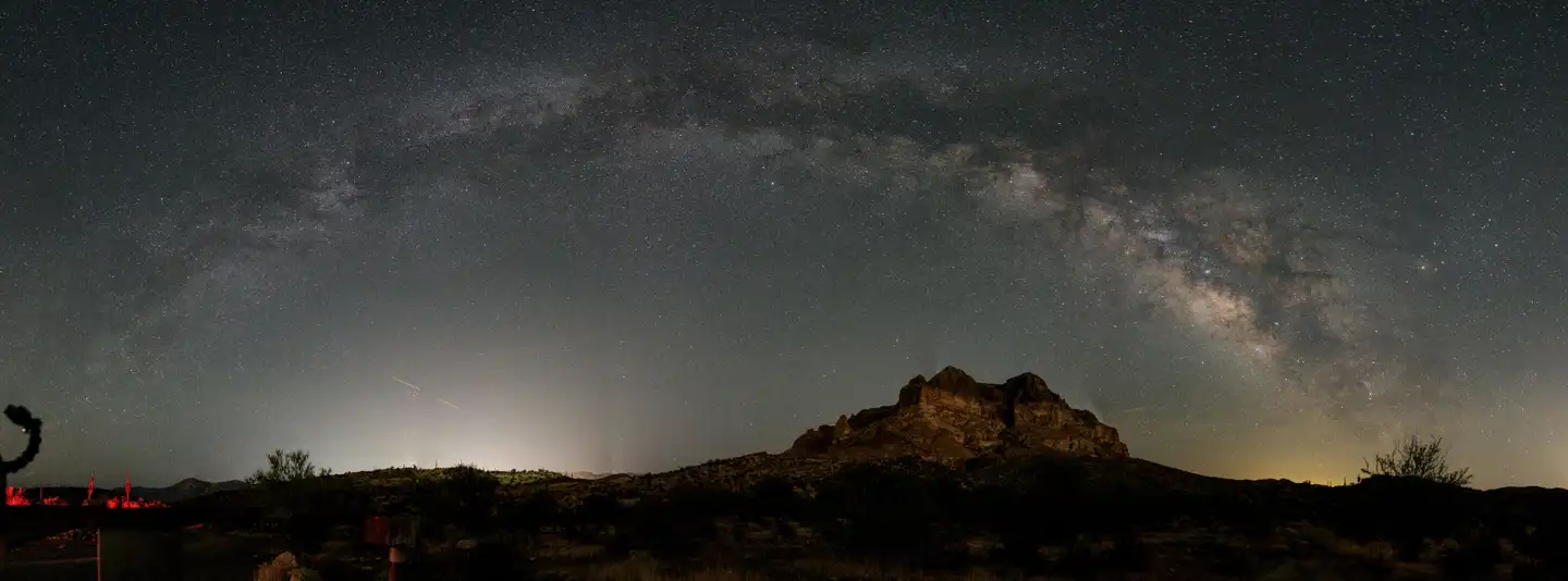 The Milky Way arching over a desert mountain silhouette, with airglow on the horizon