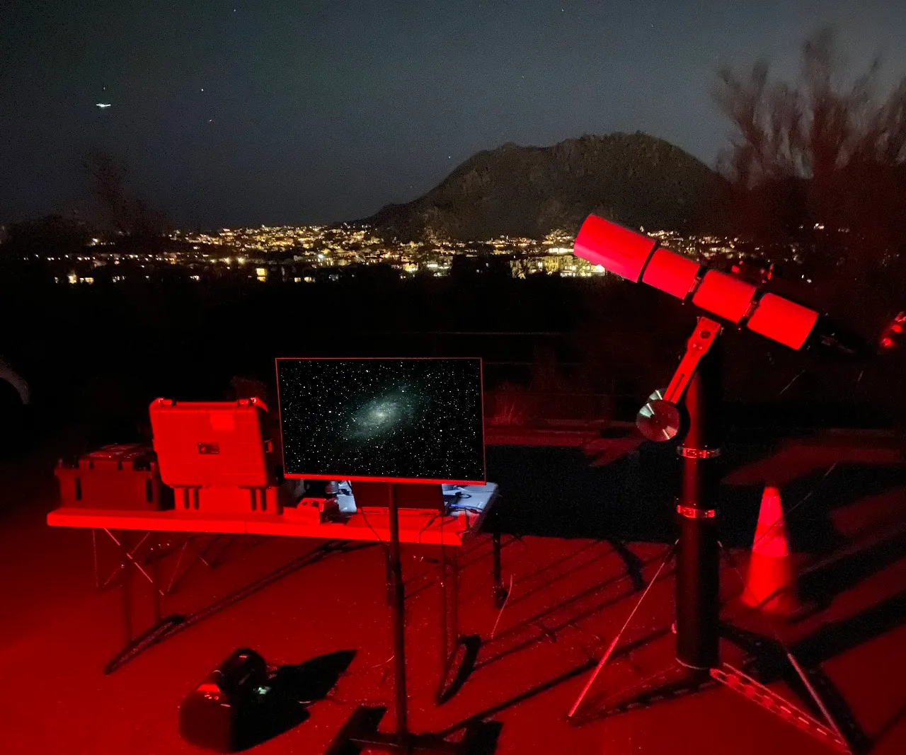 A PAS EAA telescope setup at night under red light, with the Triangulum Galaxy displayed on the monitor and the Phoenix skyline behind