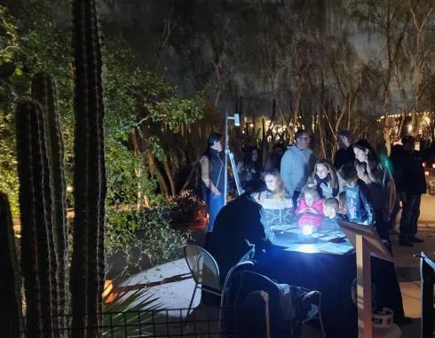A crowd gathered around a lit presentation table at a night Star Tours event