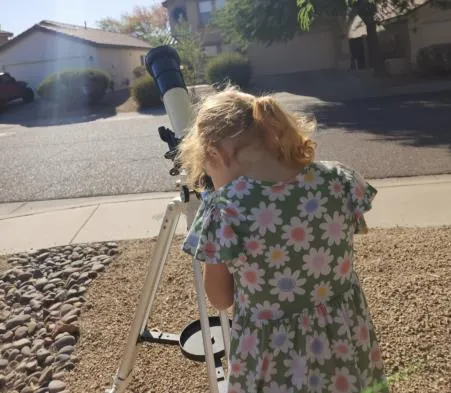 A young child looking through a visual telescope eyepiece in daylight